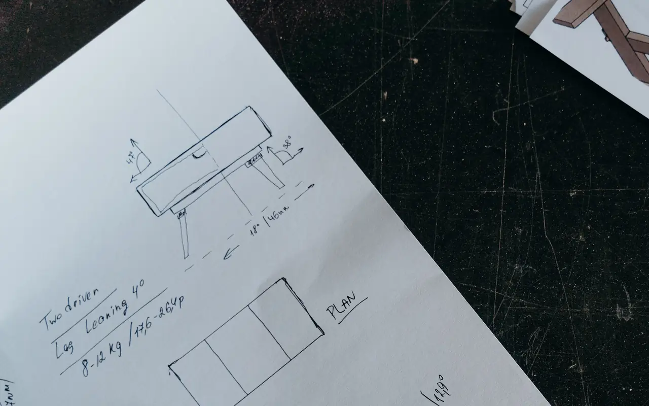 Hand-drawn product sketches with measurements on paper over a dark scratched work surface