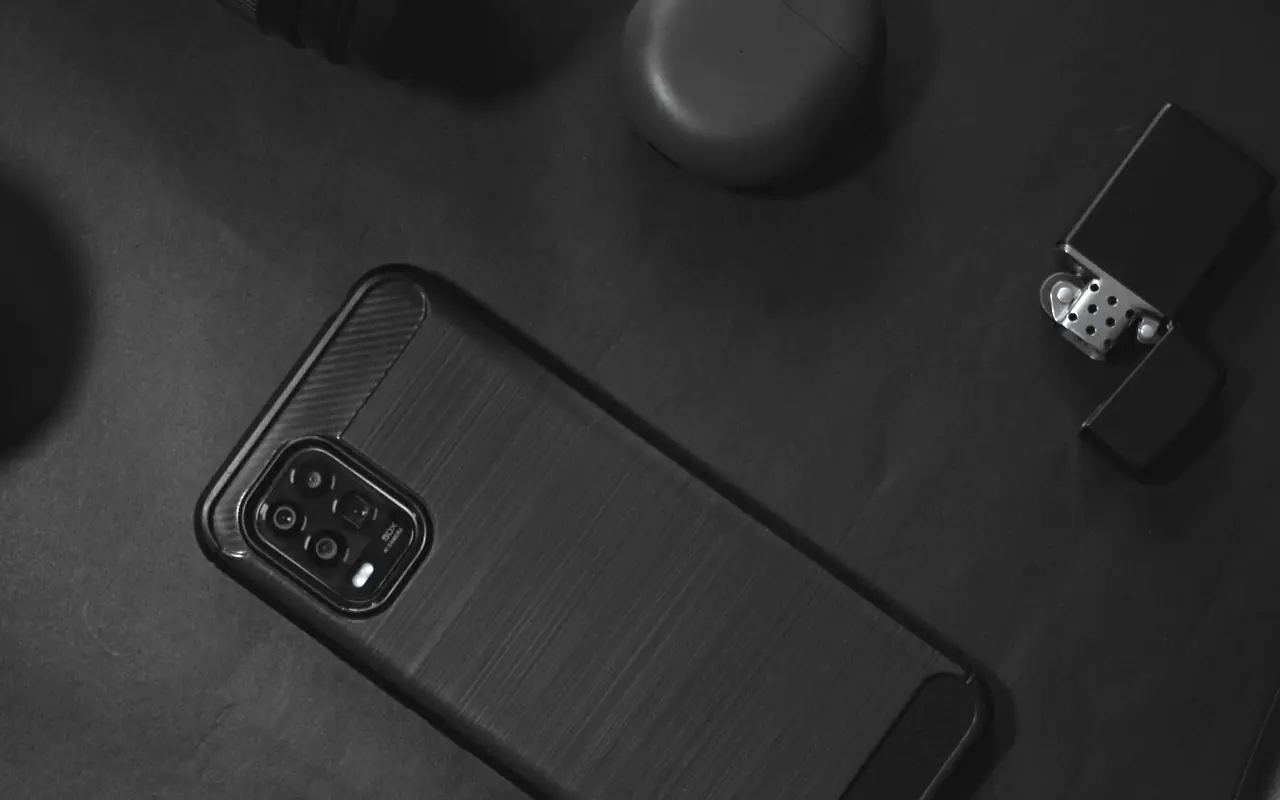 Black smartphone, earbuds case and lighter laid out on a black surface, seen from above
